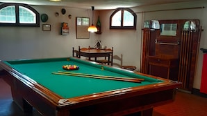 A pool table with balls, a chair, and a table lamp in a room with windows and a door.