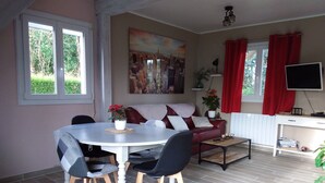 A dining area with a round table, chairs, a sofa, and a TV. - Holiday Home 'Gite En Baie De Somme' with Private Terrace, Private Garden and Wi-Fi (Saint-Quentin-en-Tourmont)