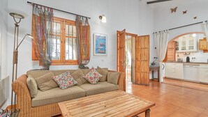 A cozy living room with a sofa, a wooden coffee table, and a kitchen area visible through an open door. - Holiday Home 'Casa Oliana' with Sea View, Pool, Garden & Wi-Fi (Competa)