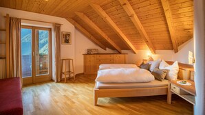 Ein Schlafzimmer mit Holzbalkendecke, einem Bett mit Kissen, einem Nachttisch und einem Fenster mit Vorhängen.