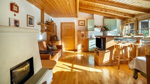 A spacious living area with a fireplace, wooden furniture, a kitchen with a large window, and a dining area with chairs. - Holiday Apartment "Adults Only Wasserfall Hegedex" with Mountain View, Balcony & Wi-Fi (Pfunders)