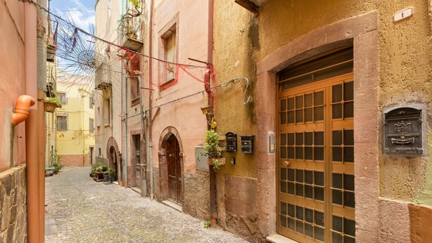 Une ruelle étroite pavée, bordée de bâtiments des deux côtés, avec une porte en bois et une fenêtre à carreaux.