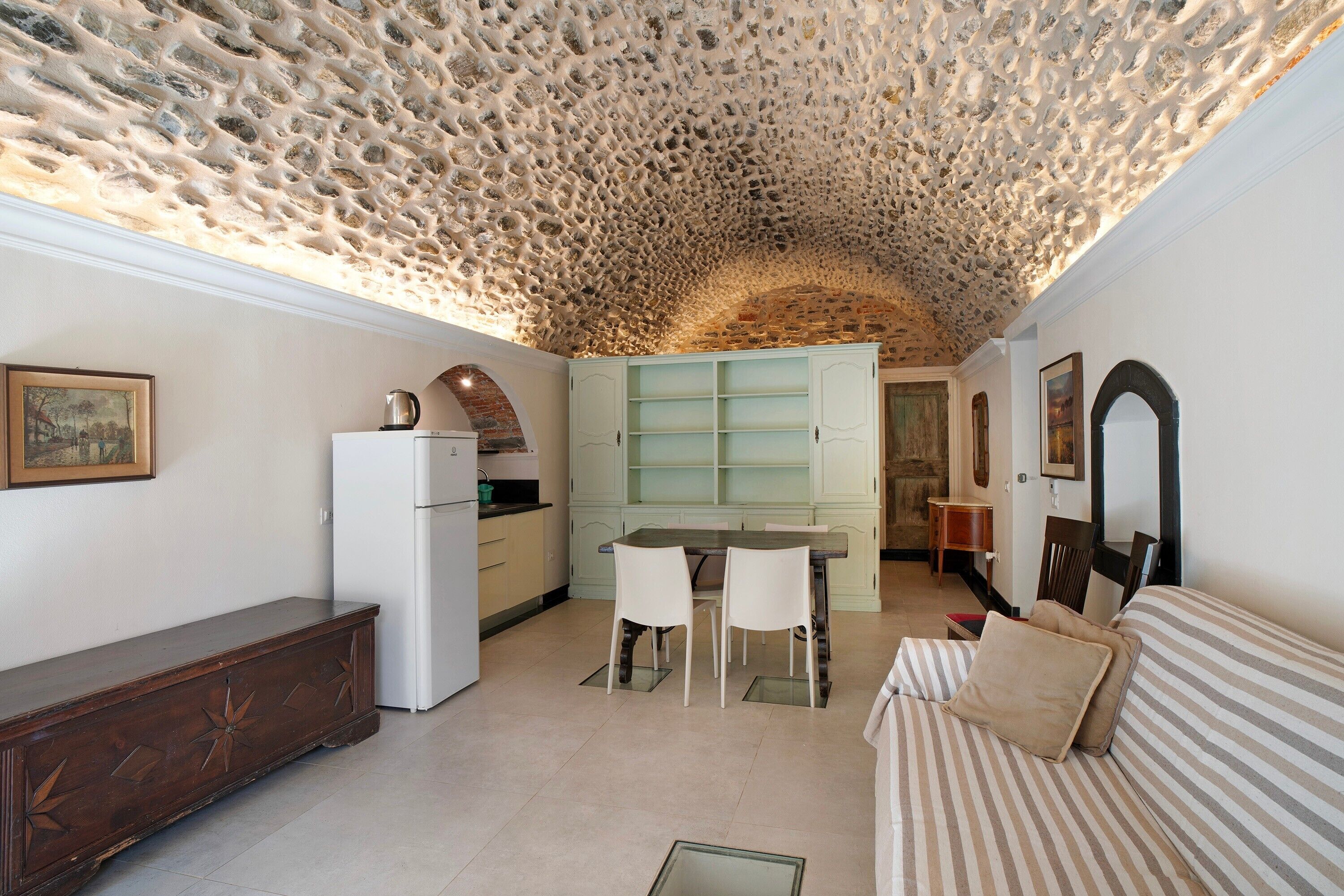 A compact kitchen with a stone ceiling, a dining area with two chairs, a white refrigerator, and a wooden cabinet.