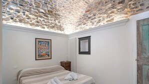 A bedroom with a stone ceiling, a bed with striped bedding, a framed painting, a bedside table, and a wooden door. - Holiday Apartment 'La Credenza, Borgo Dei Pescatori' with Wi-Fi (Cervo)