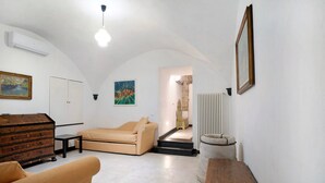 A living room with a sofa, a wooden chest of drawers, a radiator, and a staircase leading to another room.