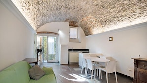 Un espacio habitable compacto con techo de piedra, una kitchenette, una zona de comedor con sillas blancas y un sofá verde.
