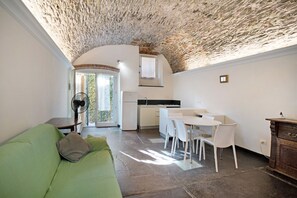 Um espaço de estar compacto com teto de pedra, uma kitchenette, zona de refeições com cadeiras brancas e um sofá verde.
