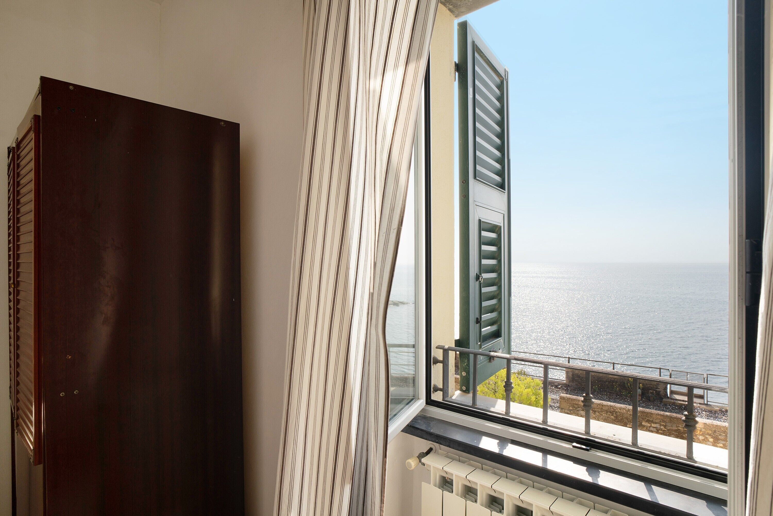 A room with a view of the sea, a radiator, and a dark wooden door.
