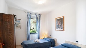 A room with two beds, a window with curtains, a lamp, and a framed picture on the wall. - Apartment 'Sardegnoli, Borgo Dei Pescatori' in Cervo, near the Beach (Cervo)