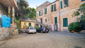 A courtyard with two cars parked, a stone wall, and a building with green shutters. - Ferrovia, Borgo Dei Pescatori Apartment with Sea View and Wi-Fi (Cervo)