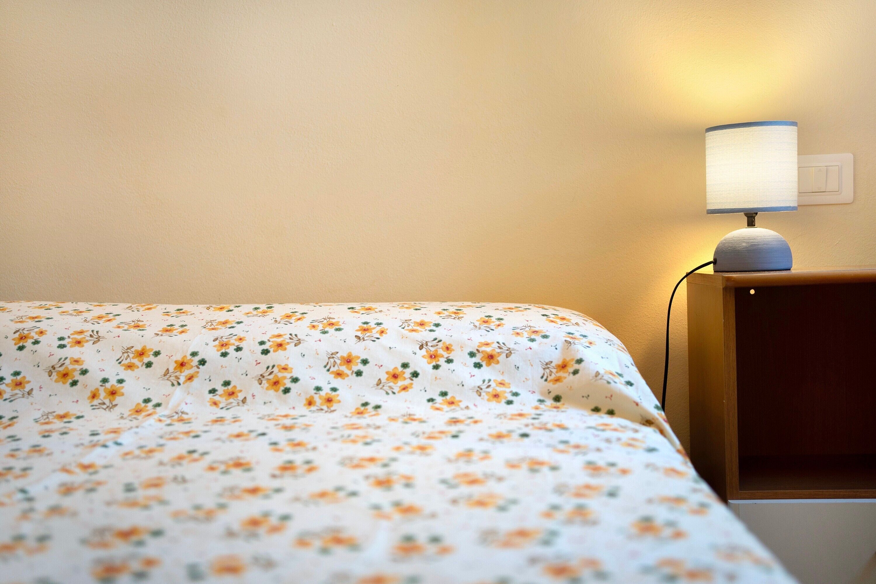 A bed with a floral bedspread, a bedside lamp, and a nightstand.
