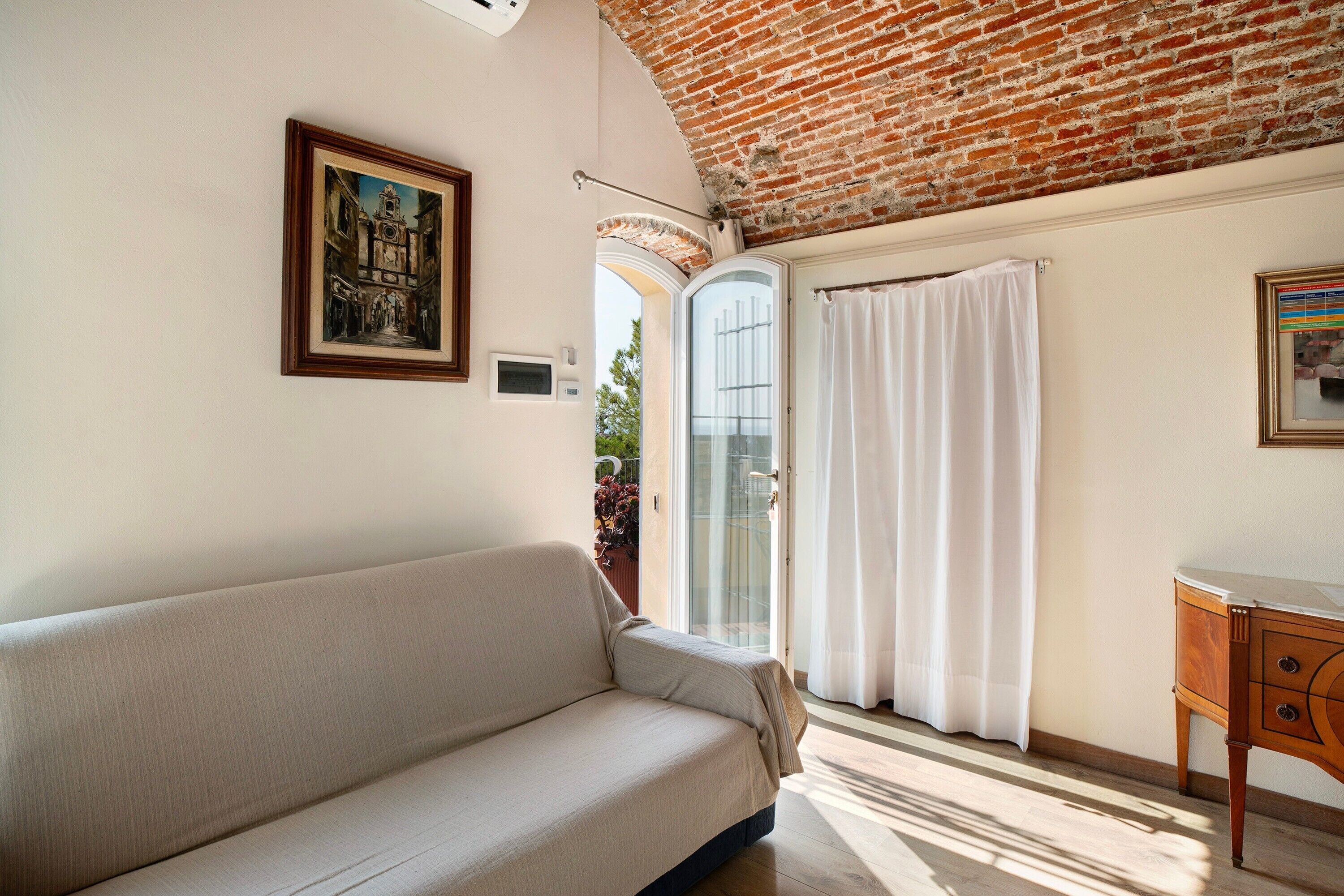A room with a sofa, a wooden cabinet, a framed picture, and a glass door leading outside.