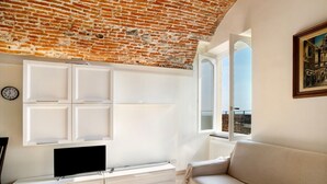 Ein Wohnzimmer mit Backstein-Decke, weißen Schränken, einem Flachbildfernseher, einer Couch und einem Fenster mit Blick.