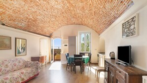 Une pièce avec un plafond en briques, un canapé, une table à manger avec des chaises, un téléviseur et des œuvres d’art accrochées aux murs.
