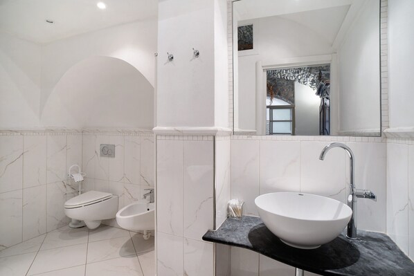A modern bathroom with a white toilet, bidet, and a large sink with a black countertop.
