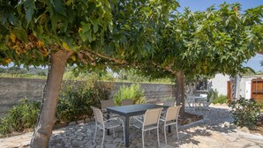Eine Terrasse im Freien mit einem Steintisch und -stühlen, umgeben von Grünpflanzen und einer Steinmauer.