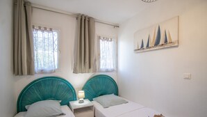 A bedroom with two beds, a nightstand, a lamp, and a sailboat painting on the wall.