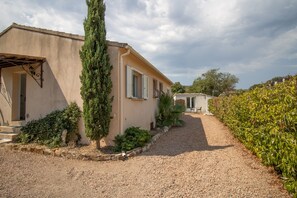A house with a gravel driveway, a tall evergreen tree, and a small building in the background.