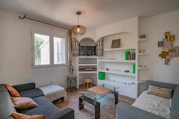 A modern living room with a sofa, a glass coffee table, a TV, and a bookshelf.