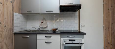 A compact kitchen with white cabinetry, a built-in oven, and a stainless steel sink.