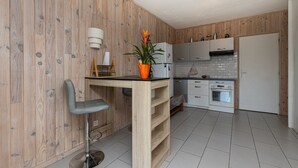A modern kitchen with wooden walls, a bar stool, a potted plant, and a built-in oven. - Studio 'Cap Breton' – adjoining house with private terrace, Wi-Fi, and air conditioning (Capbreton)