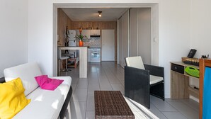 A modern living room with a sofa, a wicker chair, and a small table. A kitchen is visible in the background with wooden cabinets and a countertop. - Studio 'Cap Breton' – adjoining house with private terrace, Wi-Fi, and air conditioning (Capbreton)