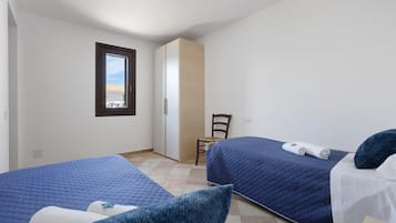 Una stanza con due letti, una sedia, una finestra e una porta.