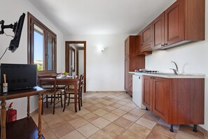 A compact kitchen with wooden cabinets, a dining table with chairs, a small refrigerator, and a window with a view. - Holiday Home "Villa Vigna" with Sea View, Pool and Wi-Fi (Badesi)