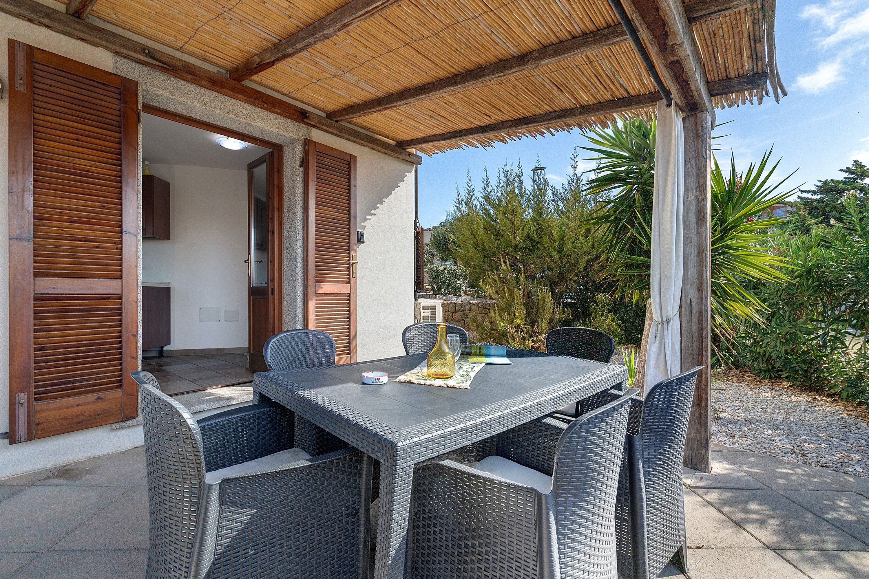 An outdoor patio with wicker furniture, a table, and a thatched roof.