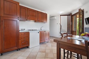 A kitchen with wooden cabinets, a built-in dishwasher, and a dining area with a table and chairs. - Holiday Home "Villa Vigna" with Sea View, Pool and Wi-Fi (Badesi)