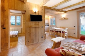 A wooden interior with a bed, a TV, a dining area, and a red sofa. - Holiday Apartment "Casa Clus Bormio 1" with Mountain View, Private Garden & Wi-Fi (Valdisotto)