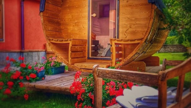 Una estructura de madera con forma de barril, con una puerta, escalones que llevan a ella y una banca afuera.