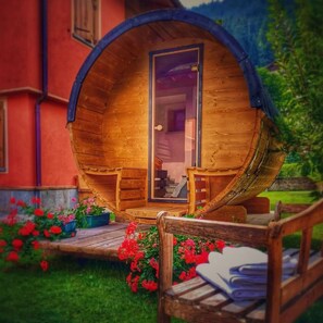 A wooden barrel-shaped structure with a door, steps leading up to it, and a bench outside. - Holiday Apartment "Casa Clus Bormio 1" with Mountain View, Private Garden & Wi-Fi (Valdisotto)