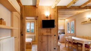 Un interior de madera con un televisor montado en la pared, un comedor con sillas y una mesa, y una cama en la habitación contigua.
