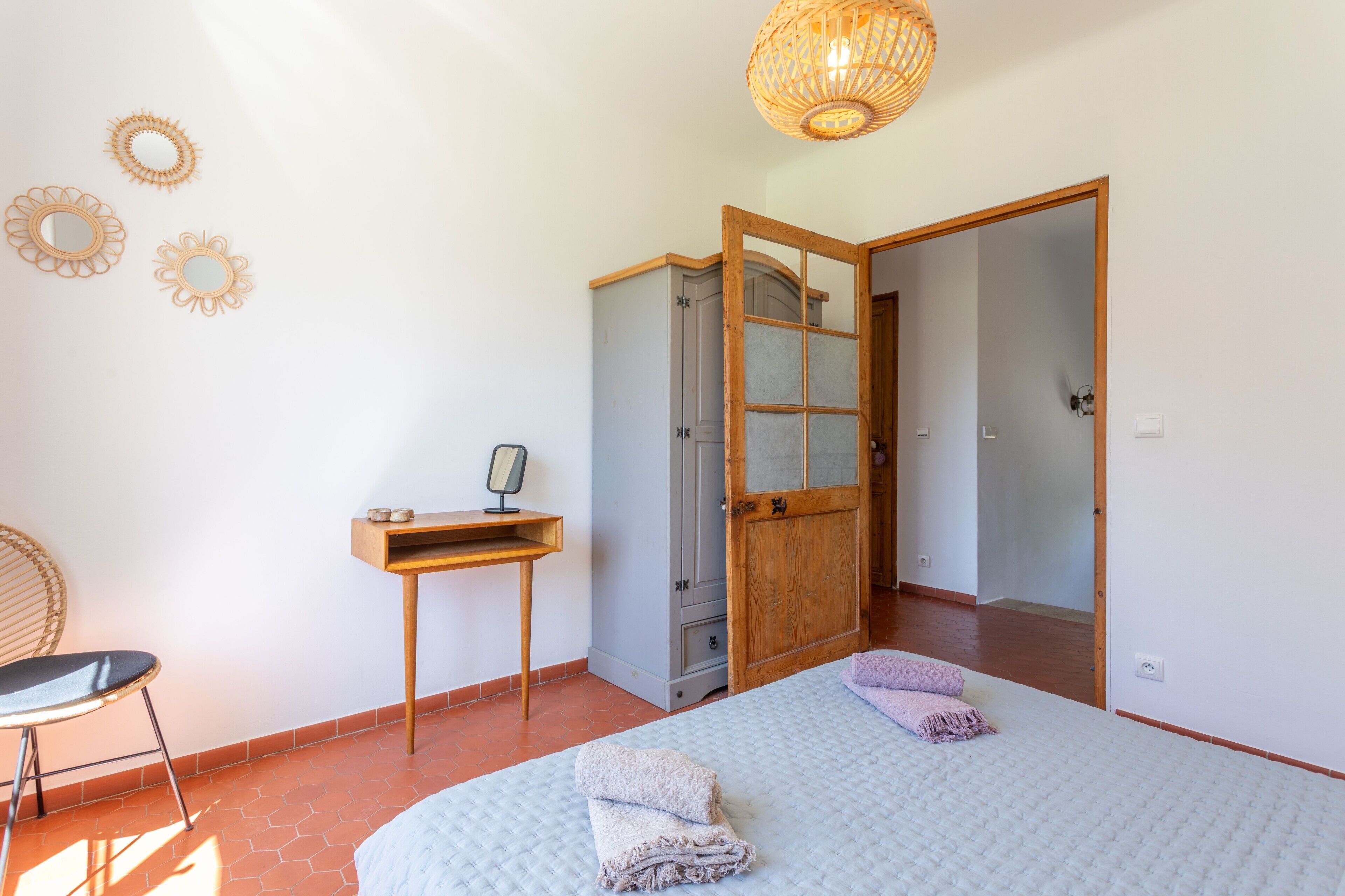 A bedroom with a bed, a desk, a chair, a wardrobe, and a door leading to another room.