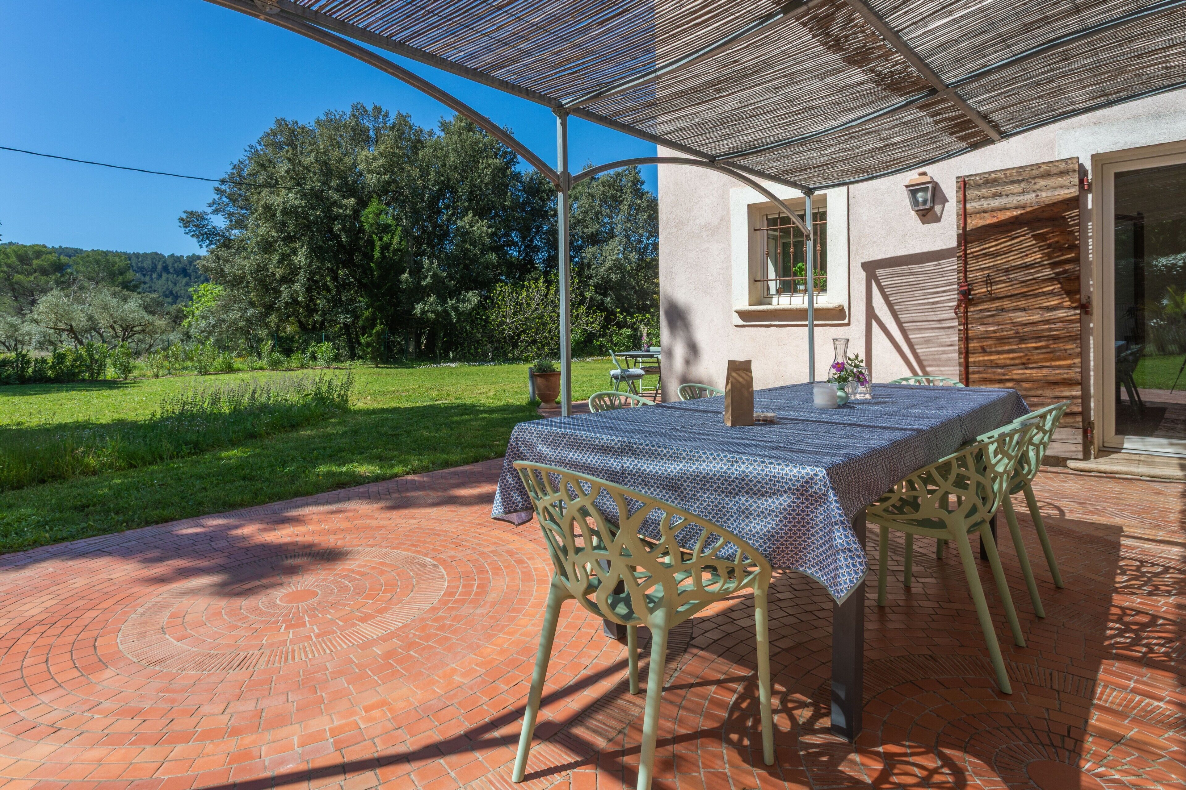 An outdoor patio with a table and chairs, a pergola, and a view of a green landscape.