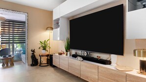 Un salon moderne avec un grand téléviseur à écran plat fixé au mur, un meuble en bois, une petite table avec une plante et un canapé.