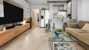 Un salon moderne avec une table basse en verre, un canapé, un téléviseur et une cuisine en arrière-plan.