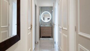 Un couloir menant à une salle de bain équipée d’un meuble-lavabo, d’un miroir et d’un luminaire rond.