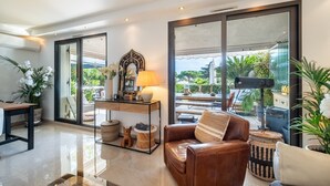 Un salon moderne avec un canapé en cuir, une table basse, une lampe et une grande fenêtre donnant sur l’extérieur.