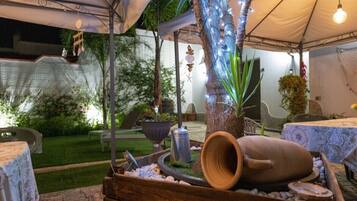 An outdoor patio area with a covered seating area, a decorative tree trunk, and a rustic wooden barrel.
