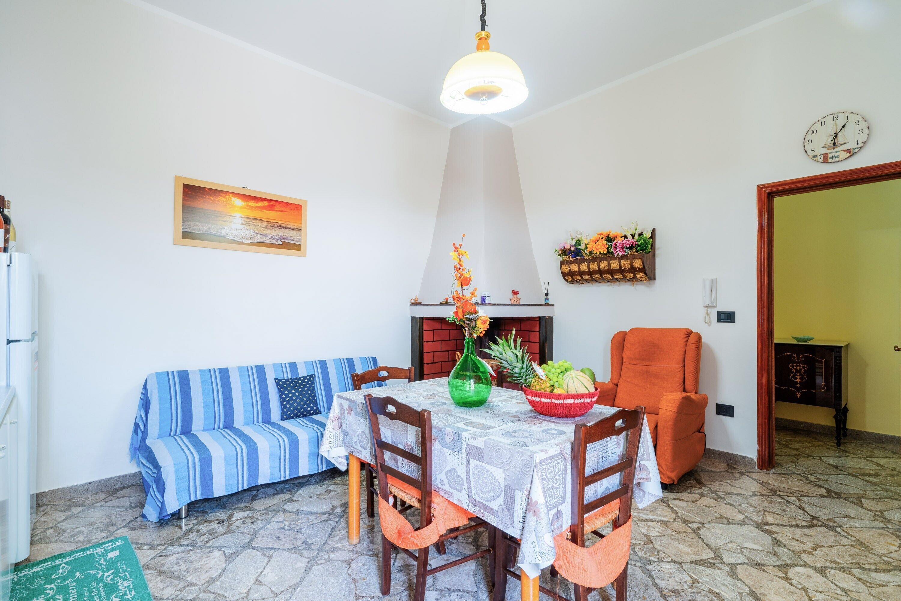 A dining area with a table set for two, a sofa, a chair, and a fireplace.