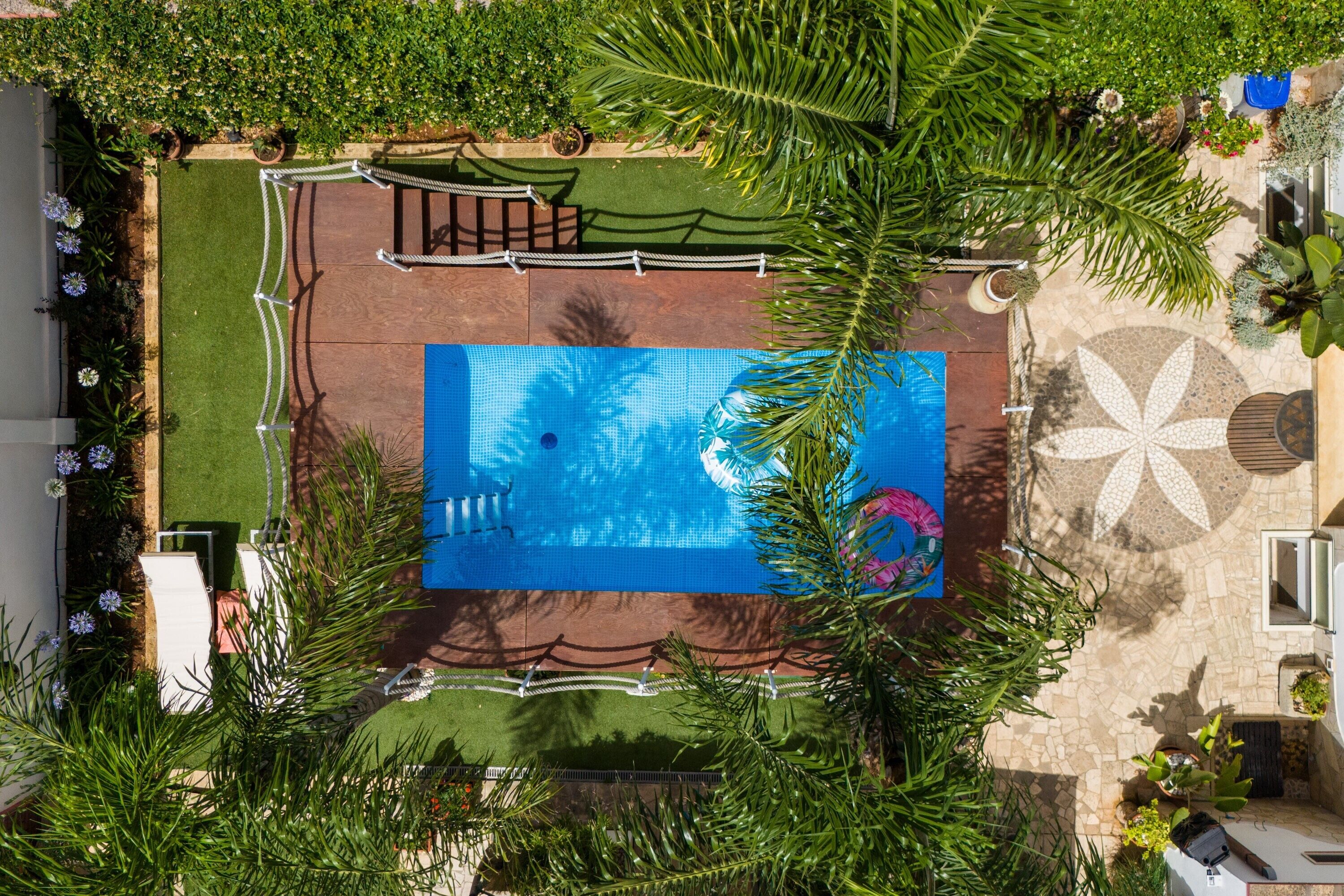An aerial view of a swimming pool surrounded by lush greenery and a patterned patio area.