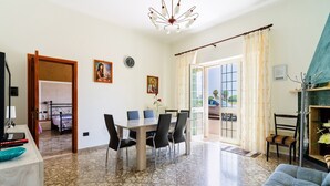 Un'ampia zona giorno con tavolo da pranzo, sedie, divano, lampadario e vista panoramica attraverso una porta in vetro.