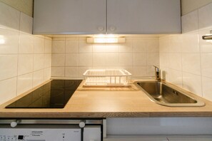 Une cuisine dotée d’une plaque de cuisson à induction noire, d’un évier en acier inoxydable et d’un lave-vaisselle situé en dessous.