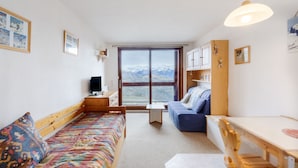 Una habitación acogedora con una cama, un sofá, una mesa de comedor y vistas a las montañas a través de un ventanal grande.