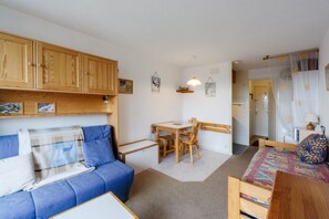 Un espacio habitable compacto con sofá, una mesita, cama, armarios de madera y una zona de cocina.