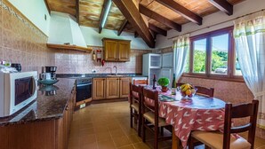 Une cuisine avec des meubles de rangement en bois, une table à manger avec des chaises et une fenêtre avec des rideaux.