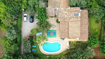 Vue aérienne d’une maison avec une piscine, deux voitures et une terrasse aménagée avec du mobilier d’extérieur.