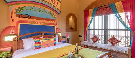 A colorful room with a bed, a bench, and a window with curtains.